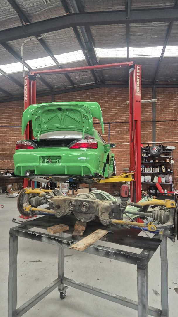 Green car raised on a workshop lift with drivetrain work underway