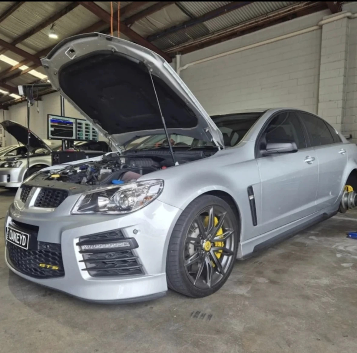 Silver GTS sedan with its bonnet open inside the workshop